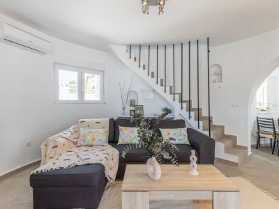 Salon lumineux avec canapé gris, escalier en pierre avec rampe noire et table basse en bois clair.