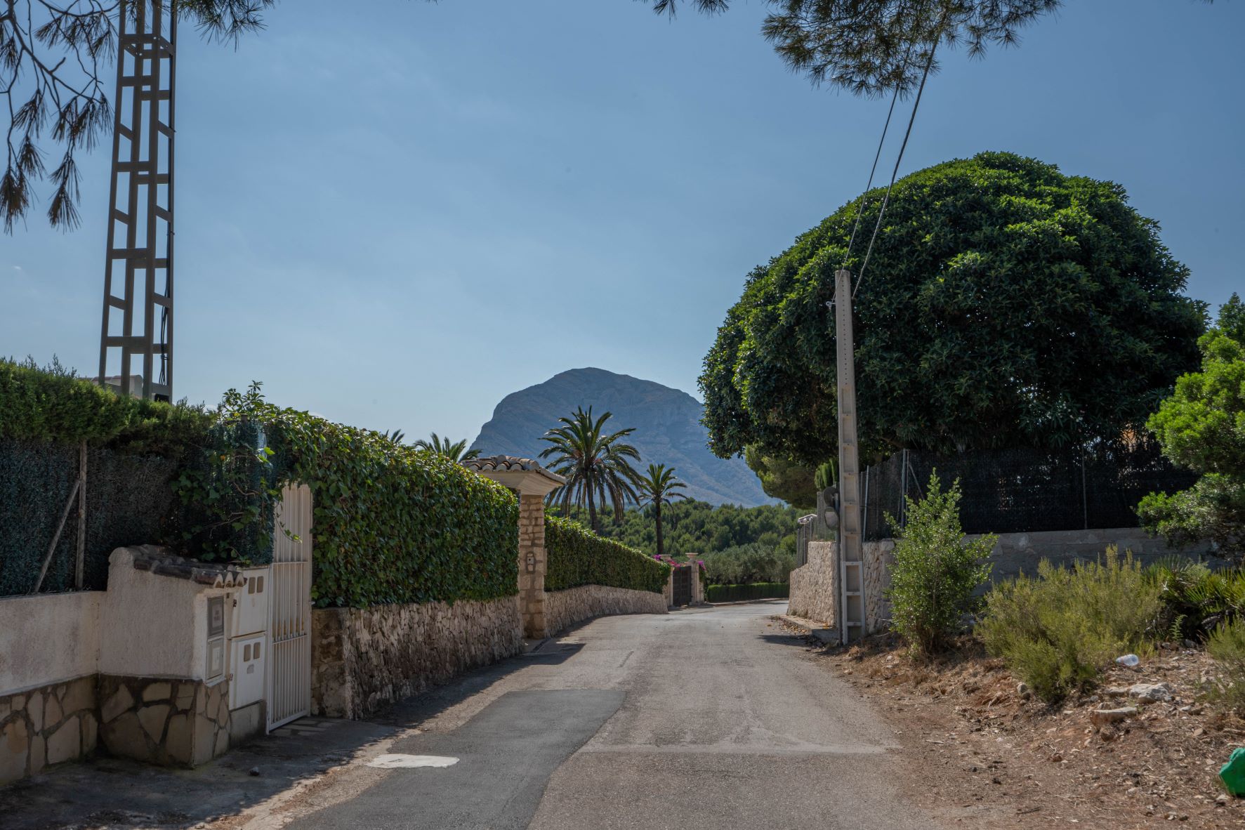 Vue de rue encadrée de murs en pierre et de verdure luxuriante, avec une montagne imposante en arrière-plan.