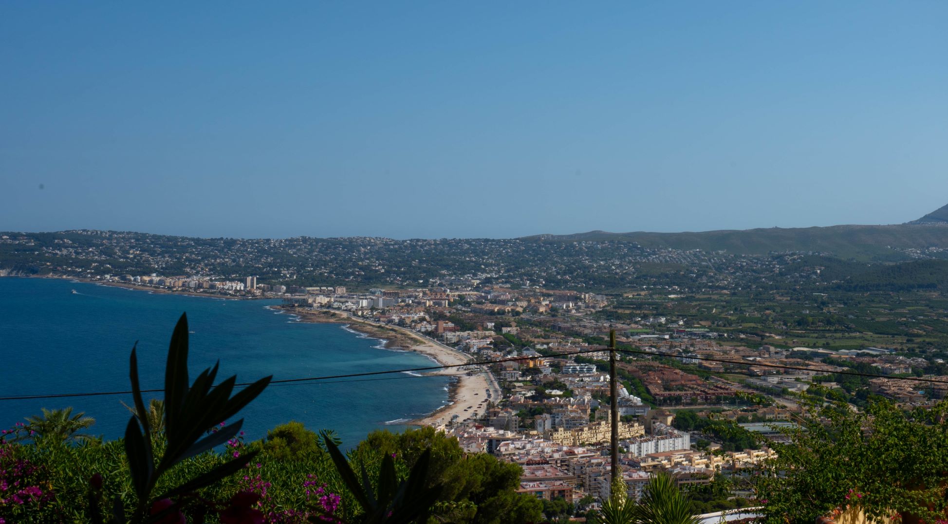 Vue panoramique sur la baie de Jávea depuis la parcelle, avec végétation au premier plan.