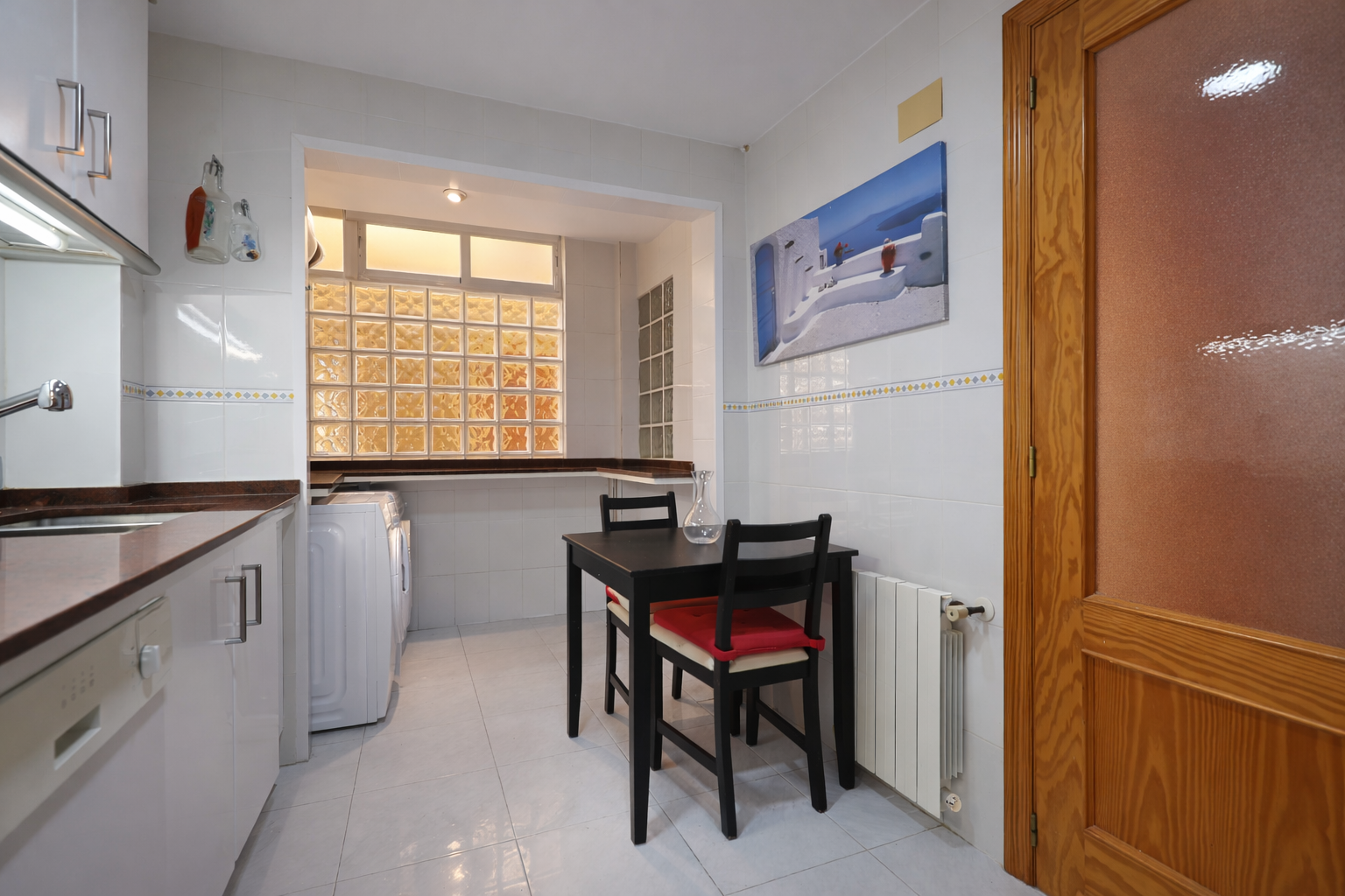 Cuisine fonctionnelle avec table à manger, électroménager blanc et fenêtre en pavés de verre.
