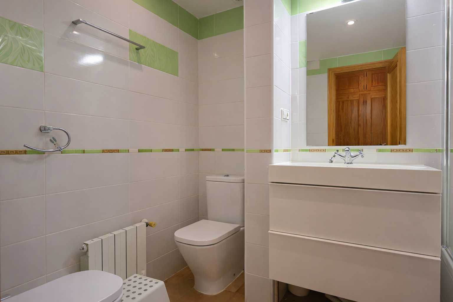 Salle de bain carrelée blanche avec détails verts, vasque moderne et miroir.