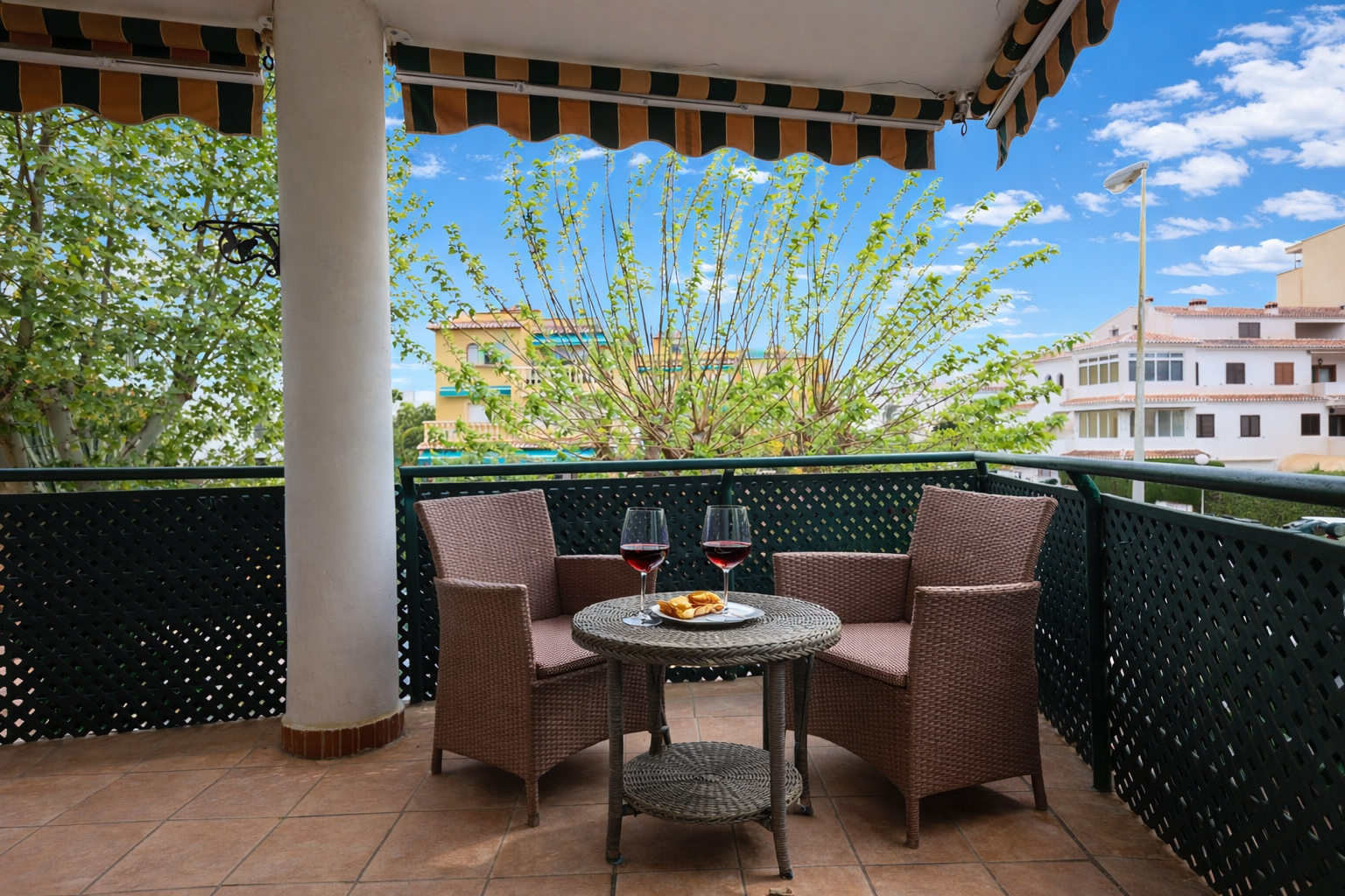 Terrasse carrelée avec store rayé et mobilier en osier offrant une vue sur l'extérieur.