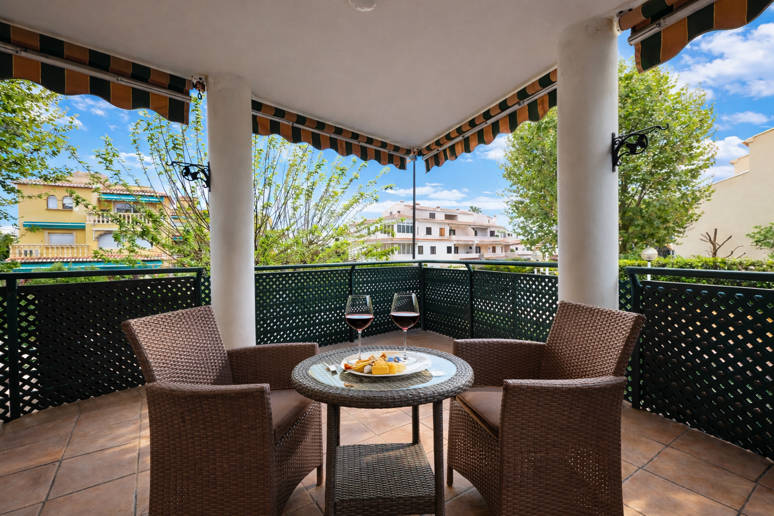 Terrasse couverte avec store rayé, table ronde avec vin et vue sur les bâtiments.