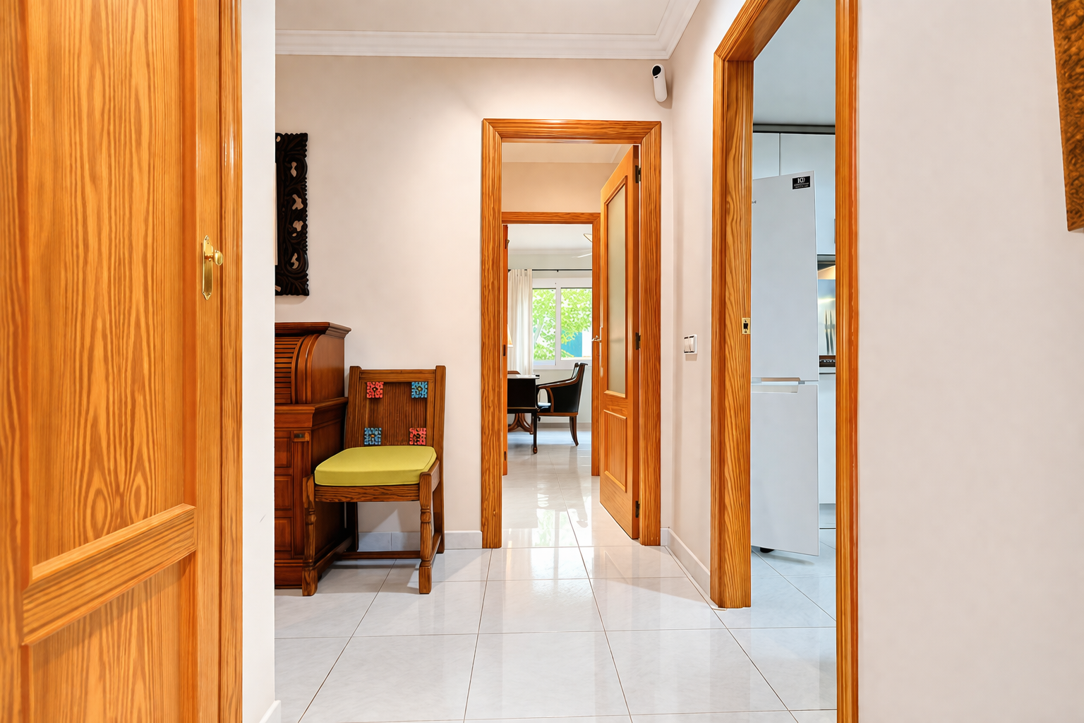 Vue du couloir avec encadrements de porte en bois et carrelage blanc.