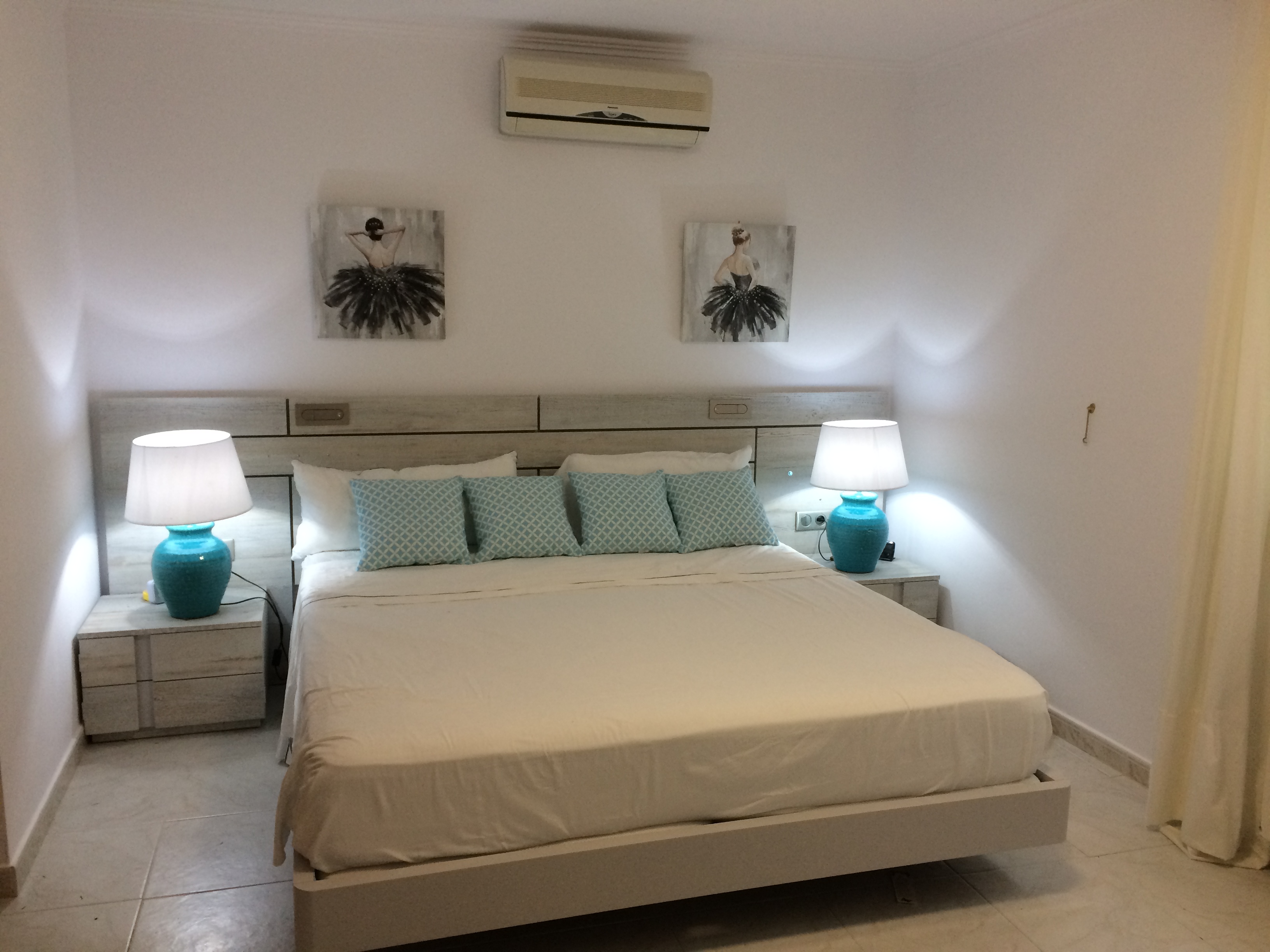 Chambre avec lit double, tête de lit en bois clair et tables de chevet assorties avec lampes en céramique bleue.