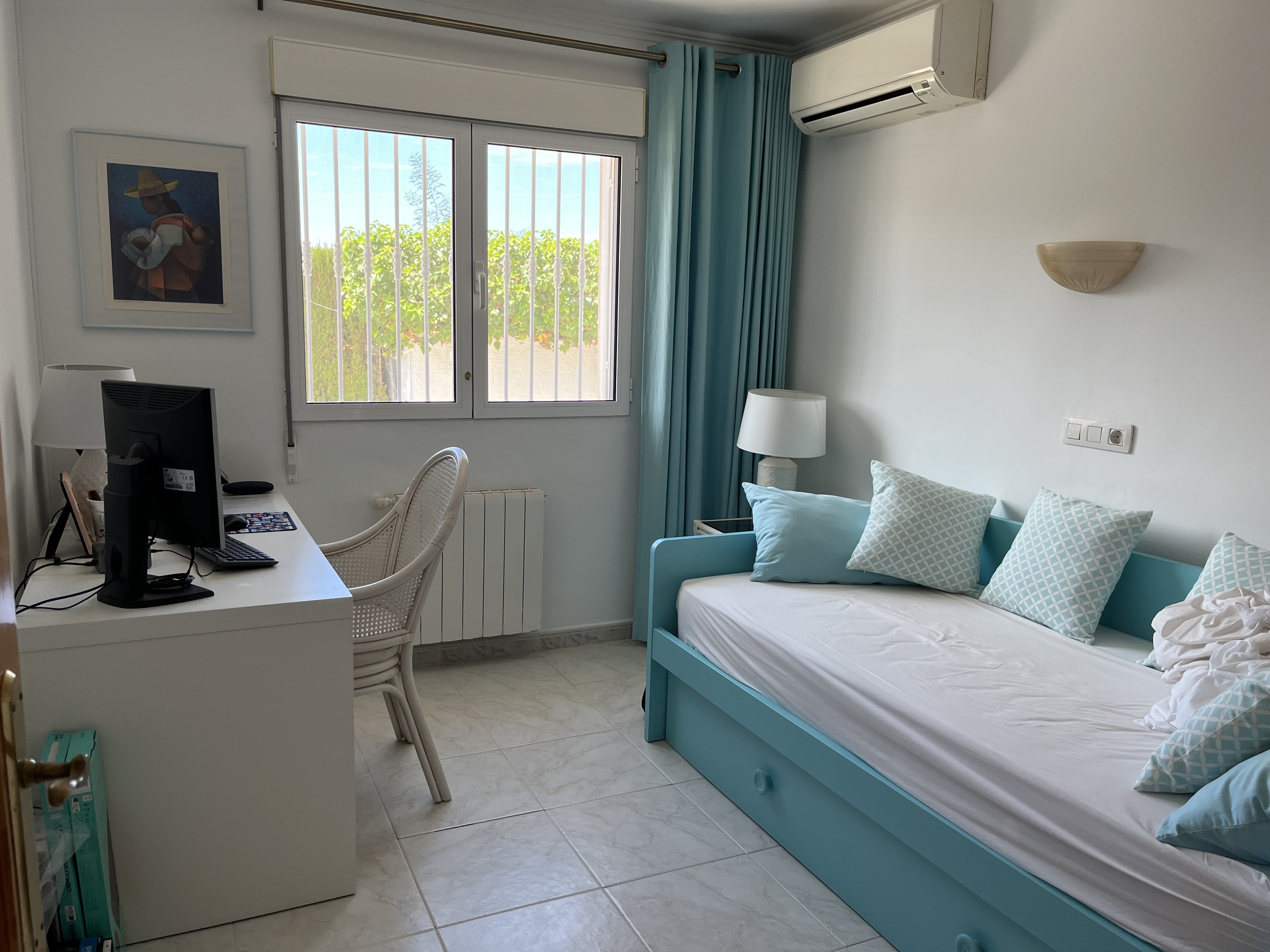 Chambre lumineuse avec lit turquoise, bureau blanc et vue sur le jardin.