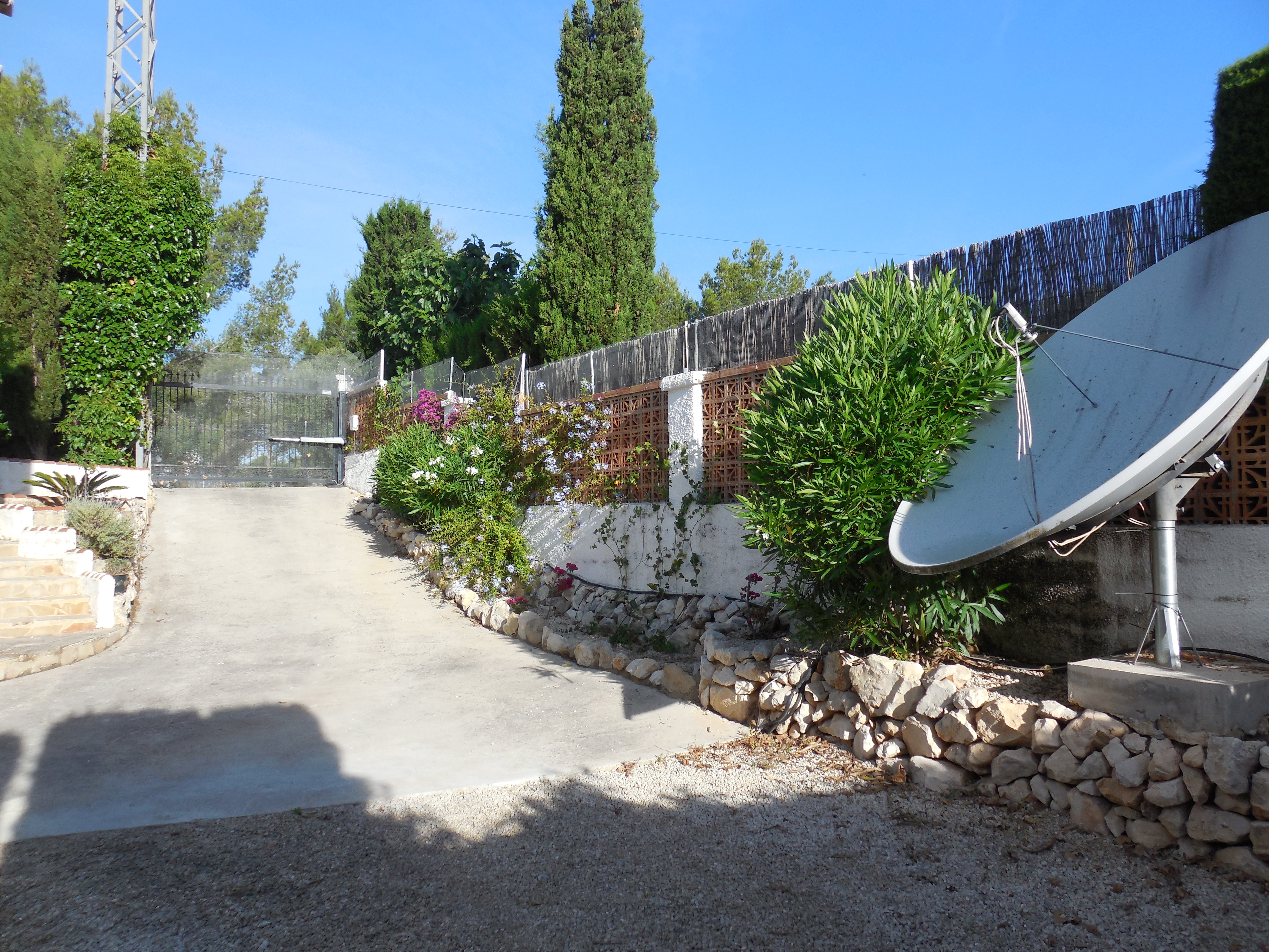 Entrée de la propriété avec allée en béton, clôture en brique et végétation luxuriante.