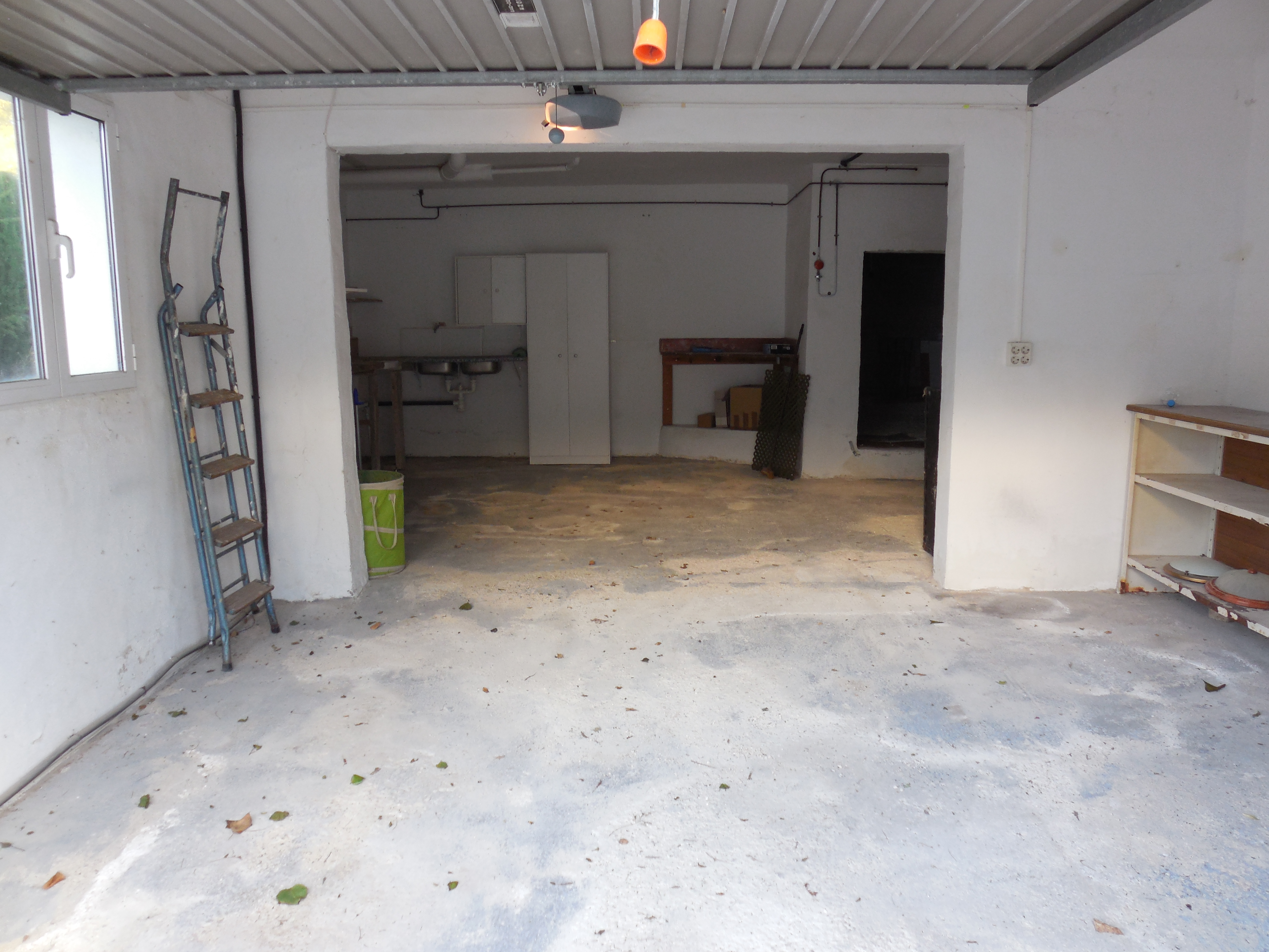 Garage avec sol en béton, murs blancs et étagères métalliques.