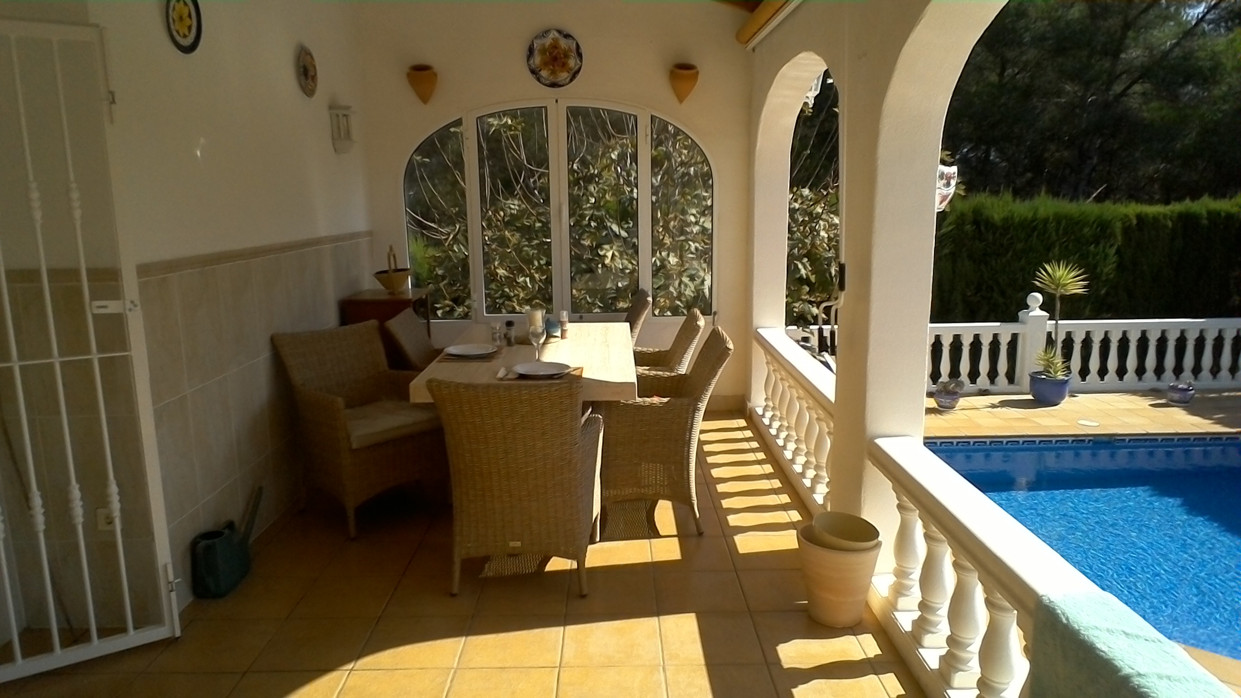 Salle à manger extérieure couverte avec vue sur la piscine et le jardin.