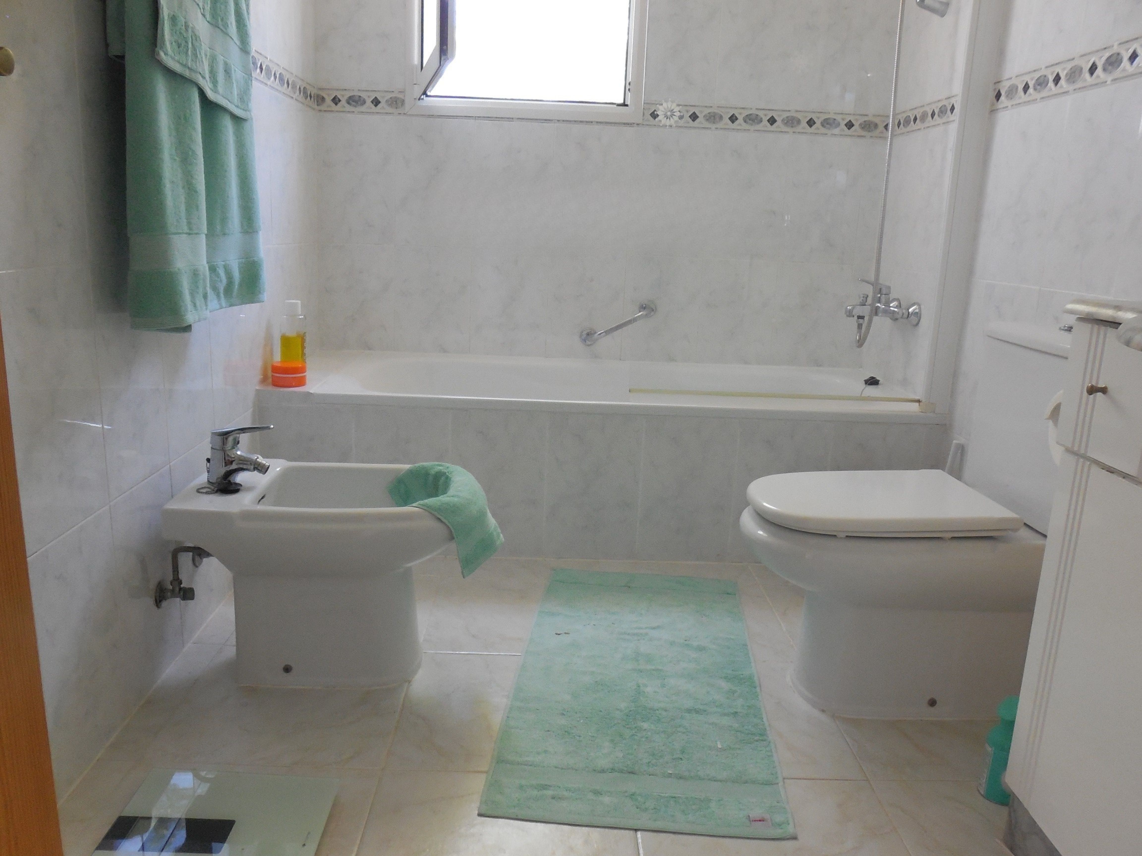 Salle de bain avec carrelage imitation marbre, baignoire, bidet et serviettes vert menthe.