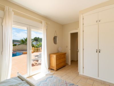 Chambre lumineuse avec accès terrasse et vue piscine. Comprend armoire intégrée et commode en bois.