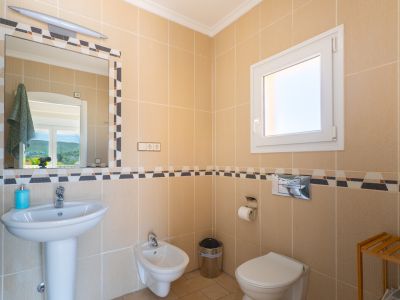 Détail de la salle de bain avec des carreaux couleur crème et une bordure décorative. Comprend un lavabo sur colonne, un bidet et des toilettes.