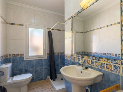 Détail de la salle de bain avec des carreaux décoratifs bleus et blancs, un lavabo sur colonne et une fenêtre.