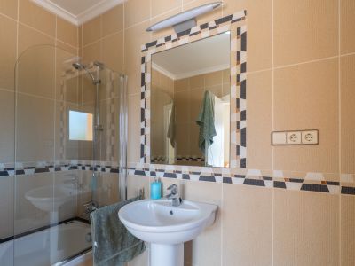 Détail de la salle de bain avec lavabo sur colonne et miroir à cadre mosaïque.