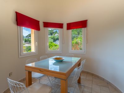 Salle à manger lumineuse avec table en verre et vue extérieure par des fenêtres à stores rouges.