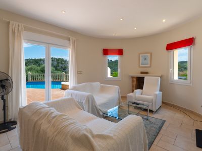 Salon lumineux avec accès terrasse et piscine. Canapés blancs recouverts et détails rouges.