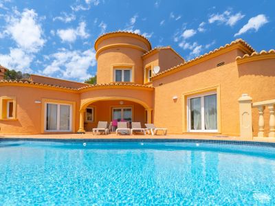 Vue de la façade principale avec piscine turquoise et terrasse avec transats.