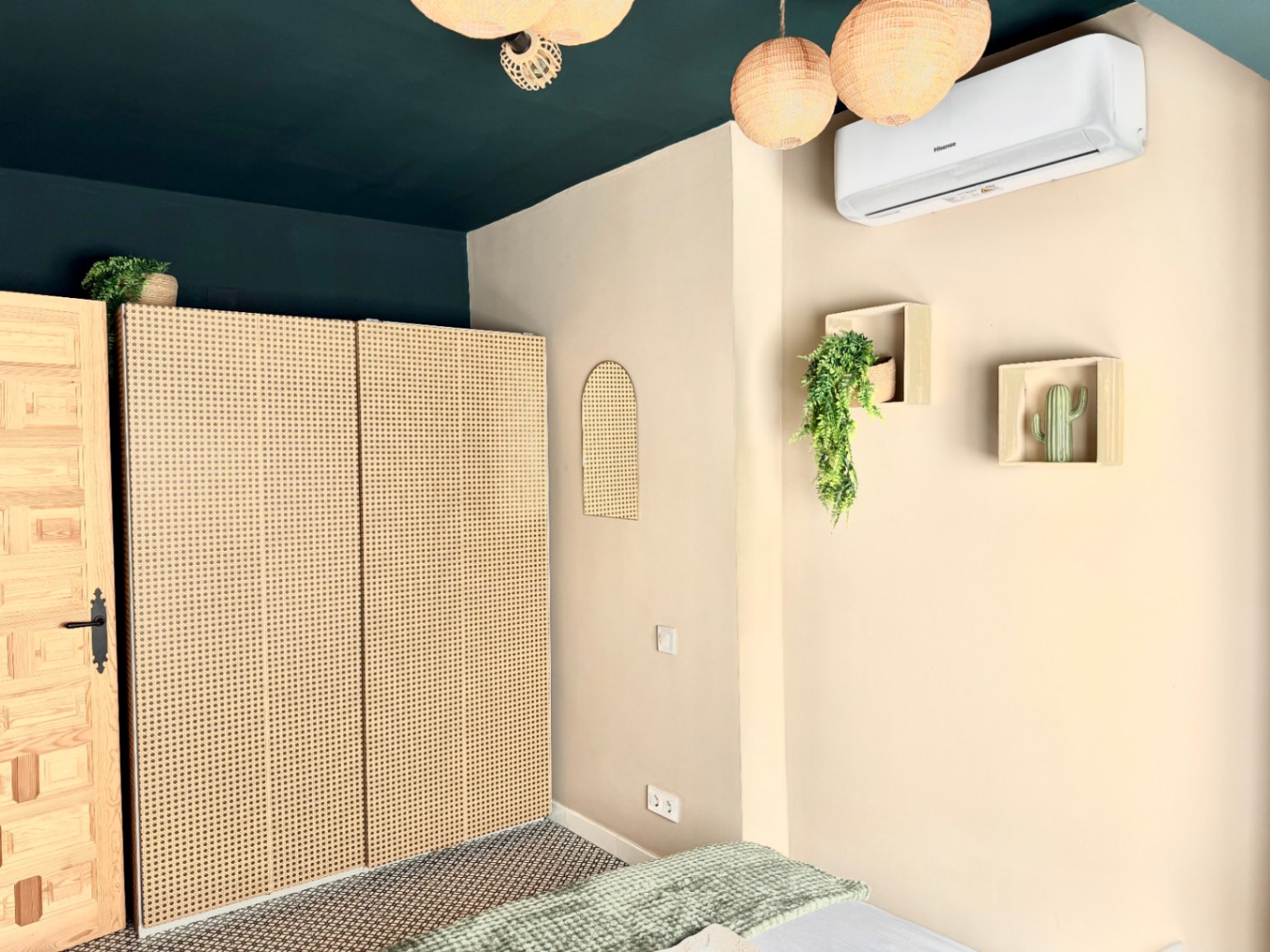 Chambre avec placard en rotin, plafond vert foncé et décoration minimaliste avec des plantes.