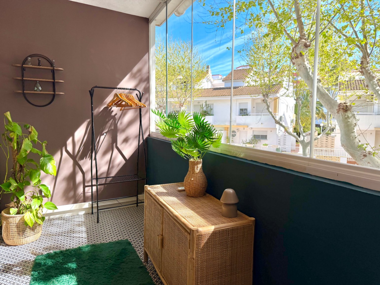 Coin intérieur lumineux avec armoire en osier et vue sur la rue depuis la fenêtre vitrée.