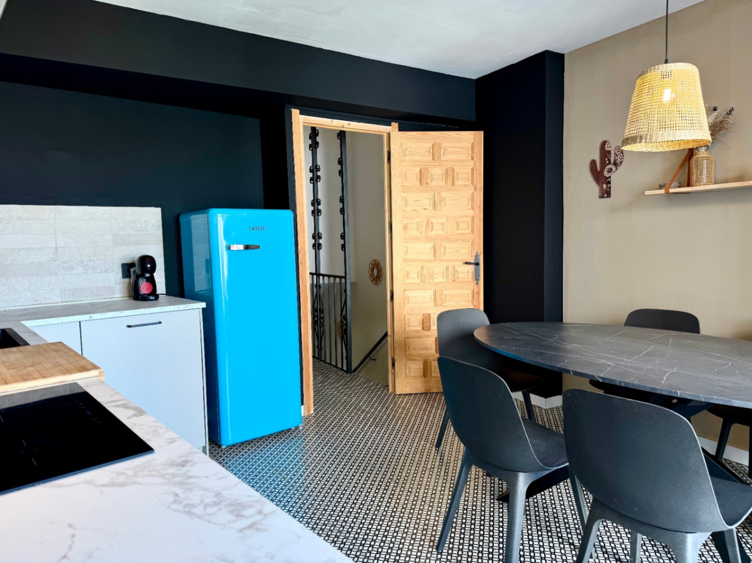 Détail de la cuisine avec réfrigérateur bleu rétro, table à manger ovale et porte en bois sculpté.