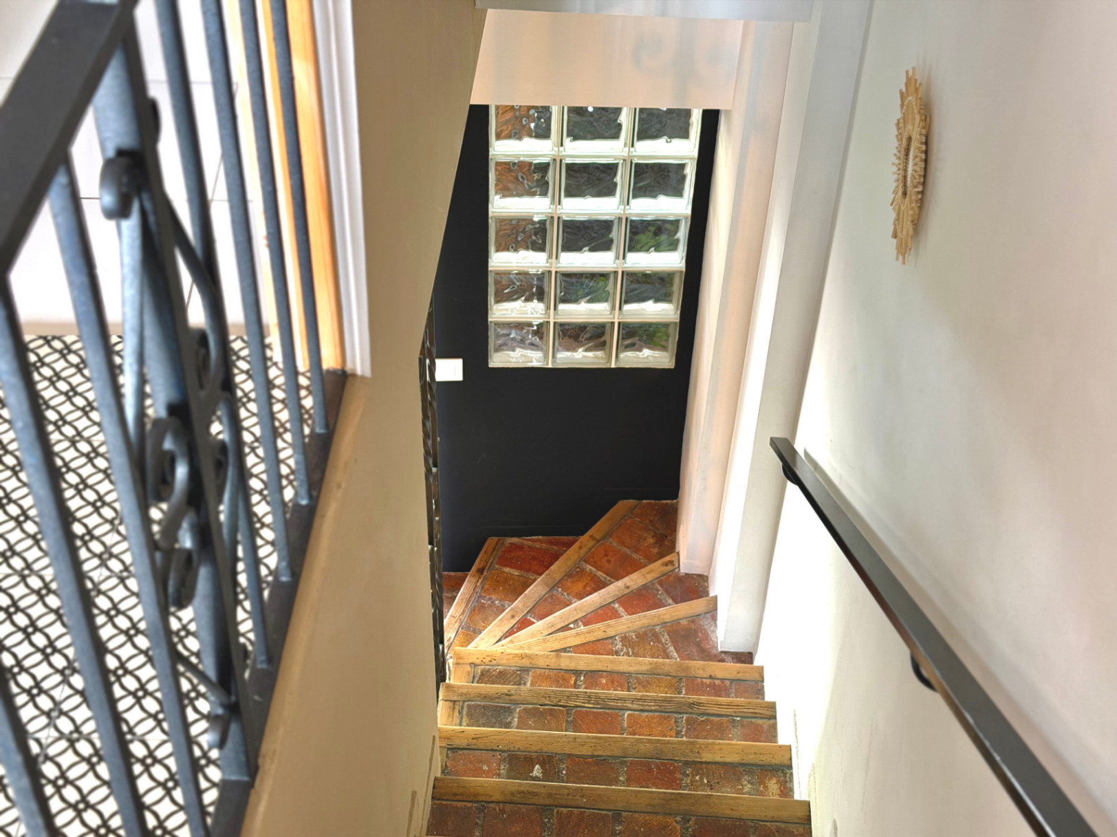 Détail de l'escalier intérieur avec rampe en fer forgé et marches en briques apparentes.