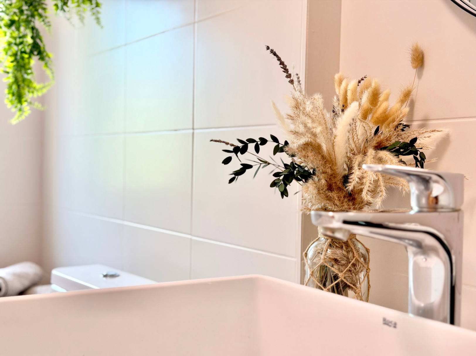 Détail de salle de bain avec lavabo blanc, robinet moderne et décor floral minimaliste.