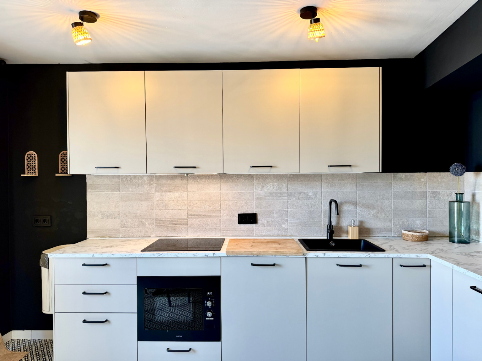 Gros plan de la cuisine rénovée avec un comptoir en marbre, des armoires claires et un mur noir contrastant.