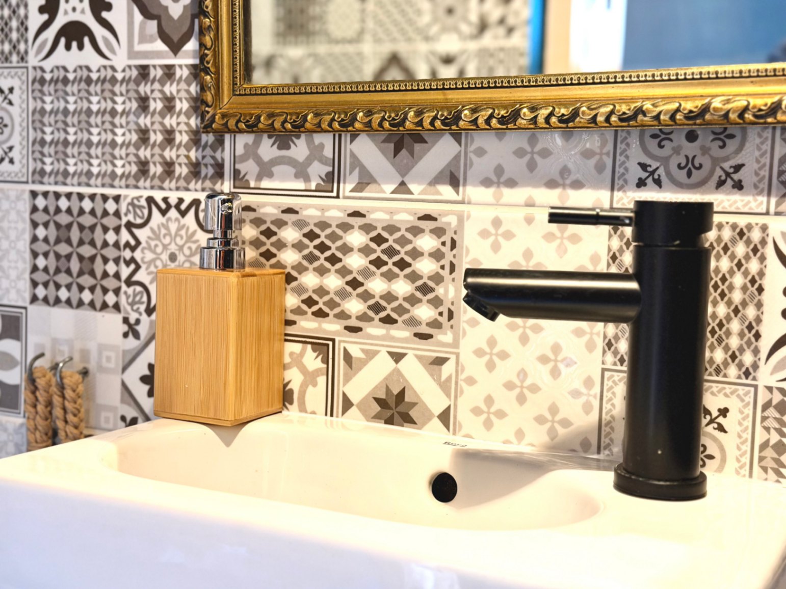 Gros plan d'un lavabo avec robinet noir mat et mosaïque décorative.