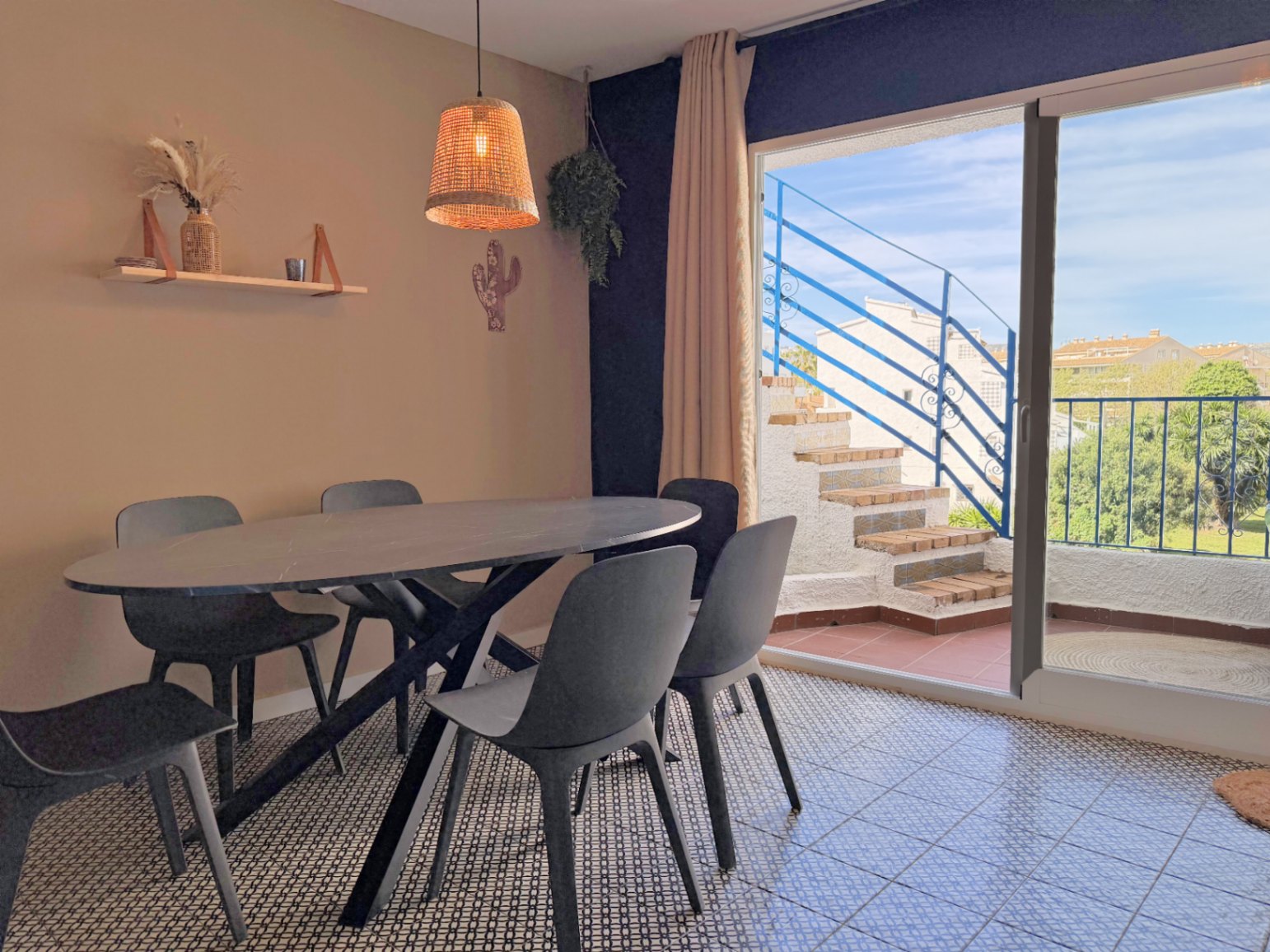 Salle à manger avec table ovale noire et accès à une terrasse extérieure avec escalier bleu.
