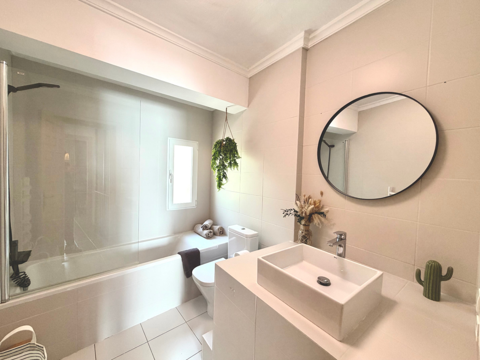 Salle de bain lumineuse avec baignoire, lavabo moderne et miroir circulaire. Décor minimaliste avec touches naturelles.