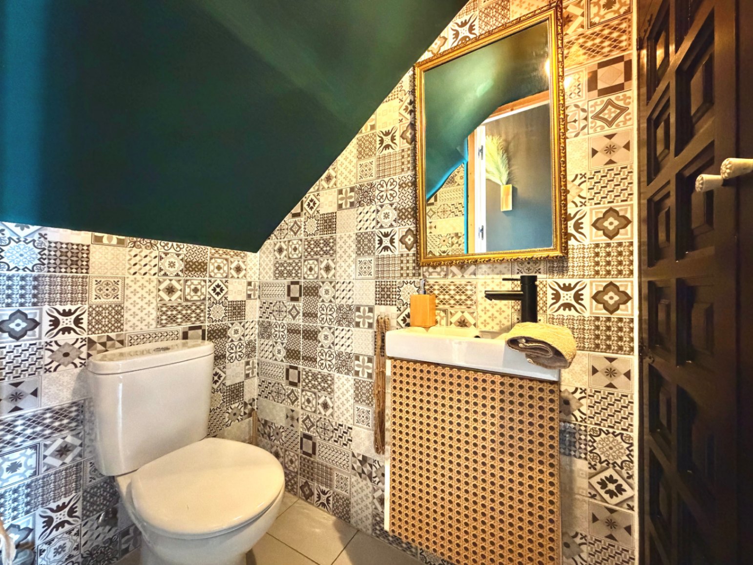 Salle d'eau avec carrelage à motifs, plafond vert foncé et meuble-lavabo en osier.