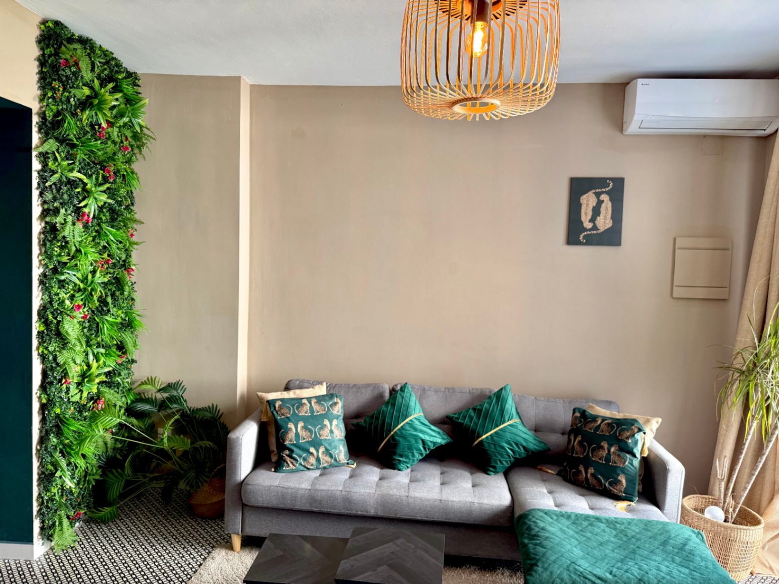 Salon moderne avec mur végétal vertical, canapé gris avec coussins verts et lampe de plafond en bois.