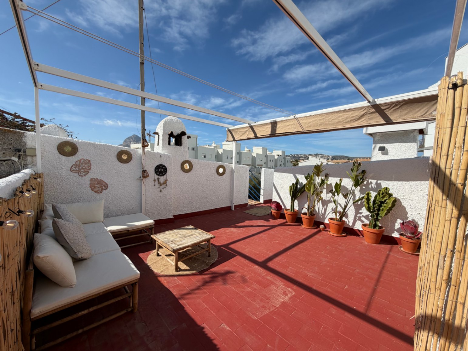 Terrasse avec sol en terre cuite, mobilier en bambou et décorations murales artisanales.