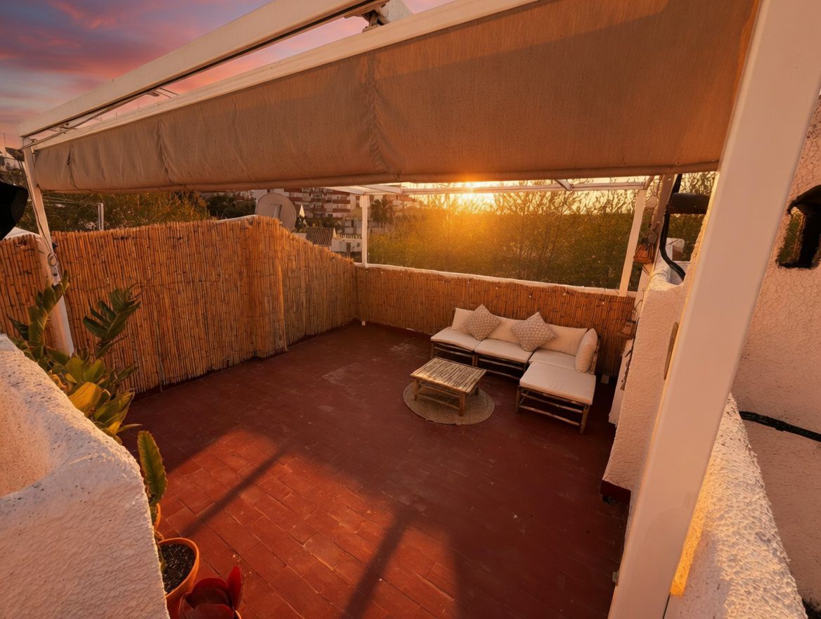 Terrasse privée avec auvent, sol en carreaux rouges et clôture en bambou. Mobilier d'extérieur et vue sur le coucher de soleil.