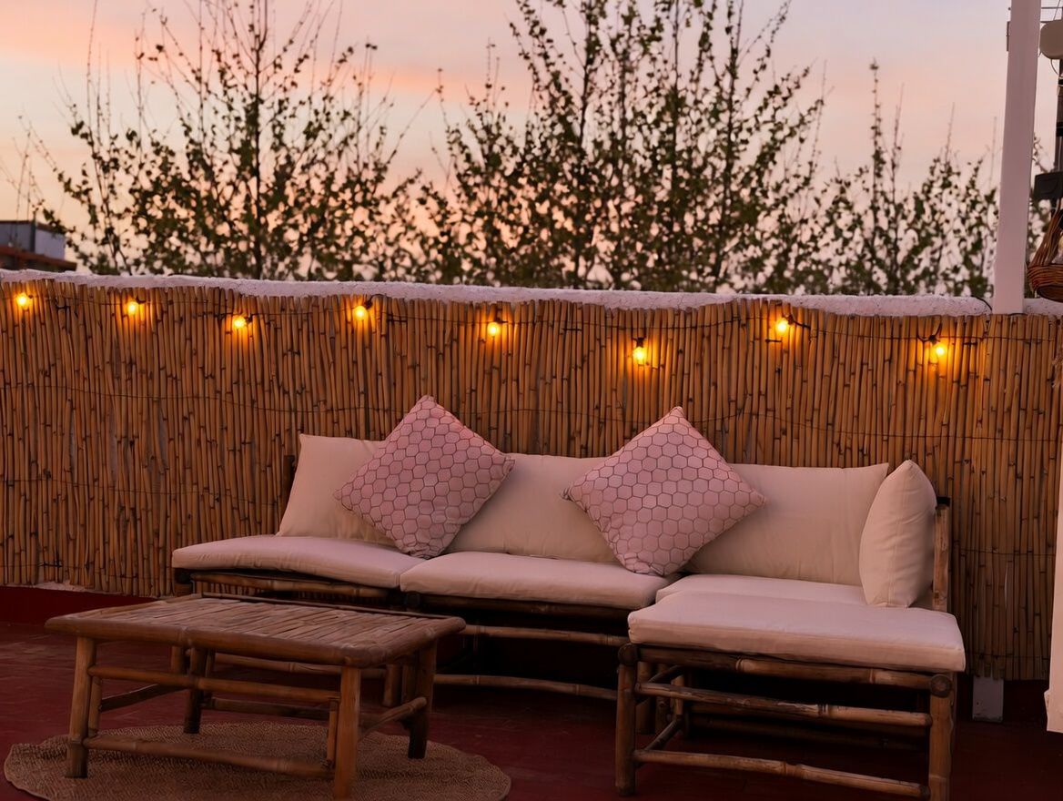 Terrasse privée avec clôture en bambou et lumières chaudes, meublée d'un canapé et d'une table basse en bambou.