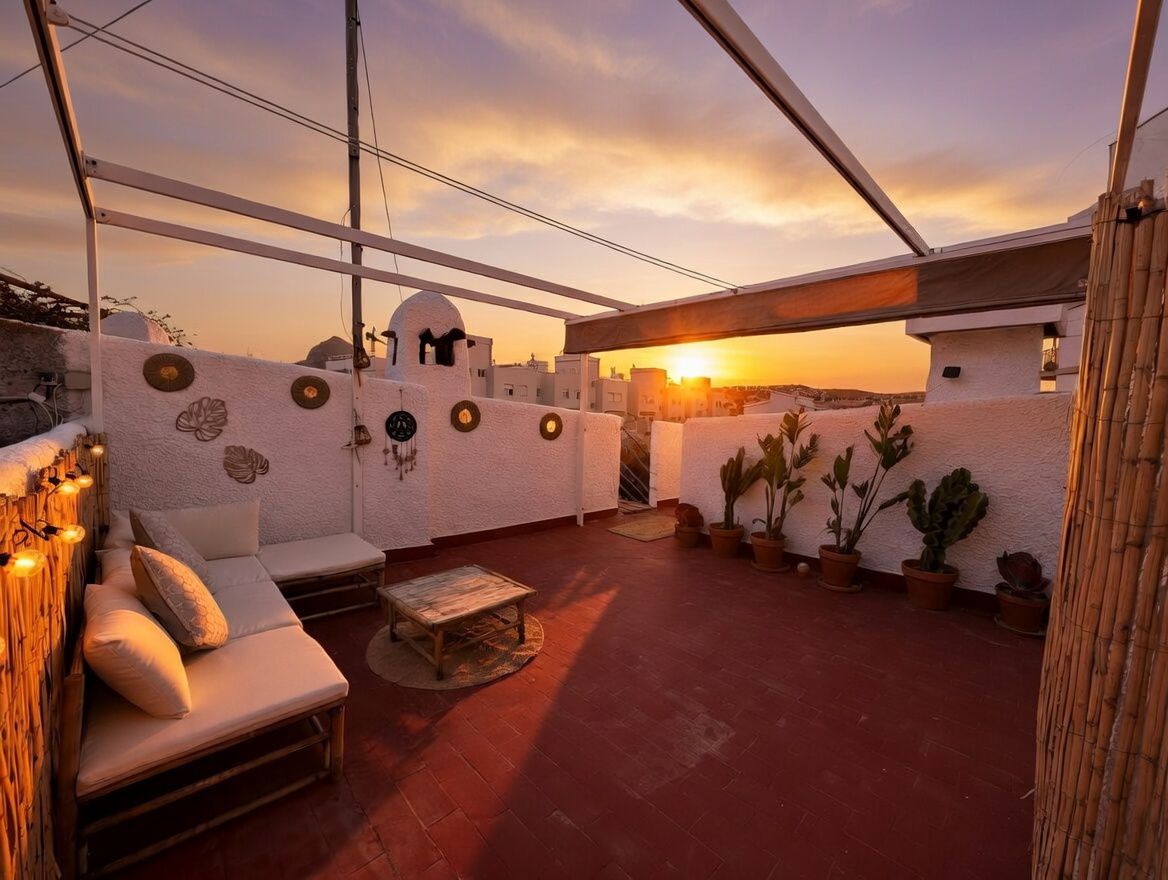 Terrasse privée sur le toit avec sol en terre cuite, plantes en pot, mobilier en bambou et vue sur le coucher du soleil.
