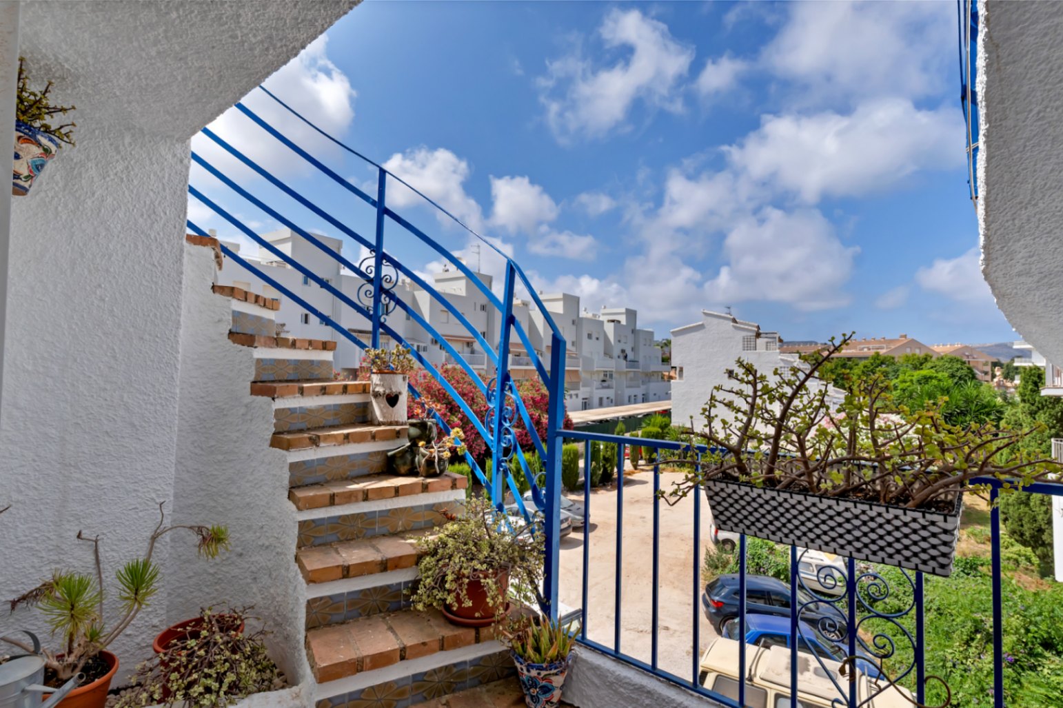 Vue de l'escalier extérieur avec rampe bleue, détails en céramique et plantes ornementales.