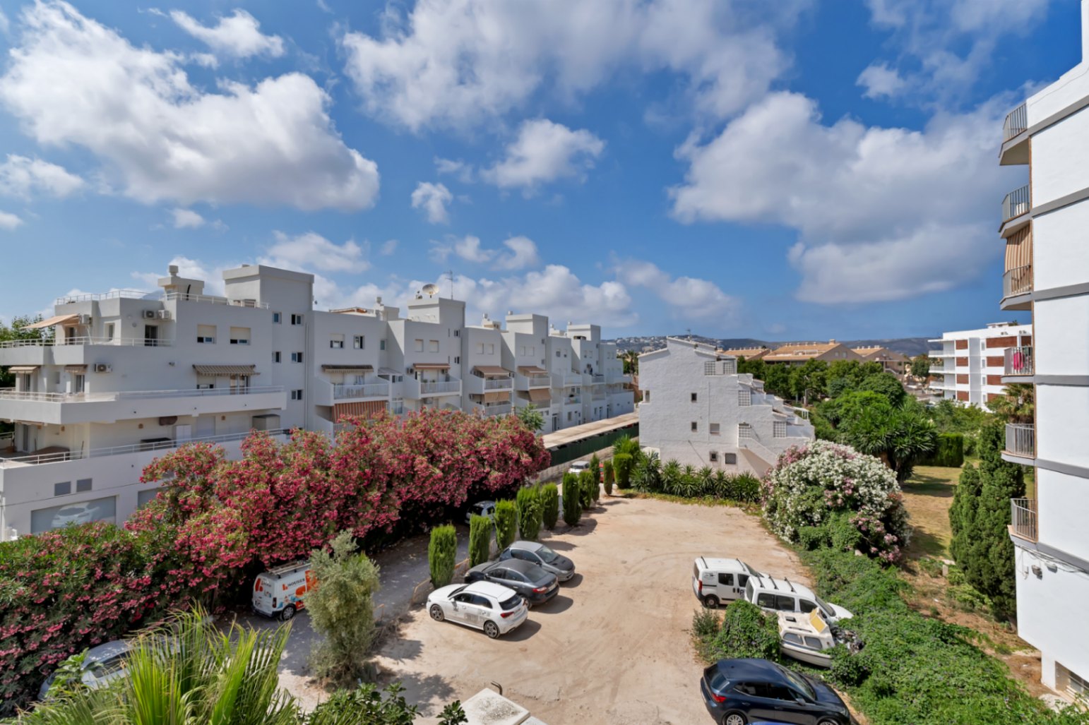 Vue surélevée du parking communautaire avec bâtiments blancs et verdure luxuriante.