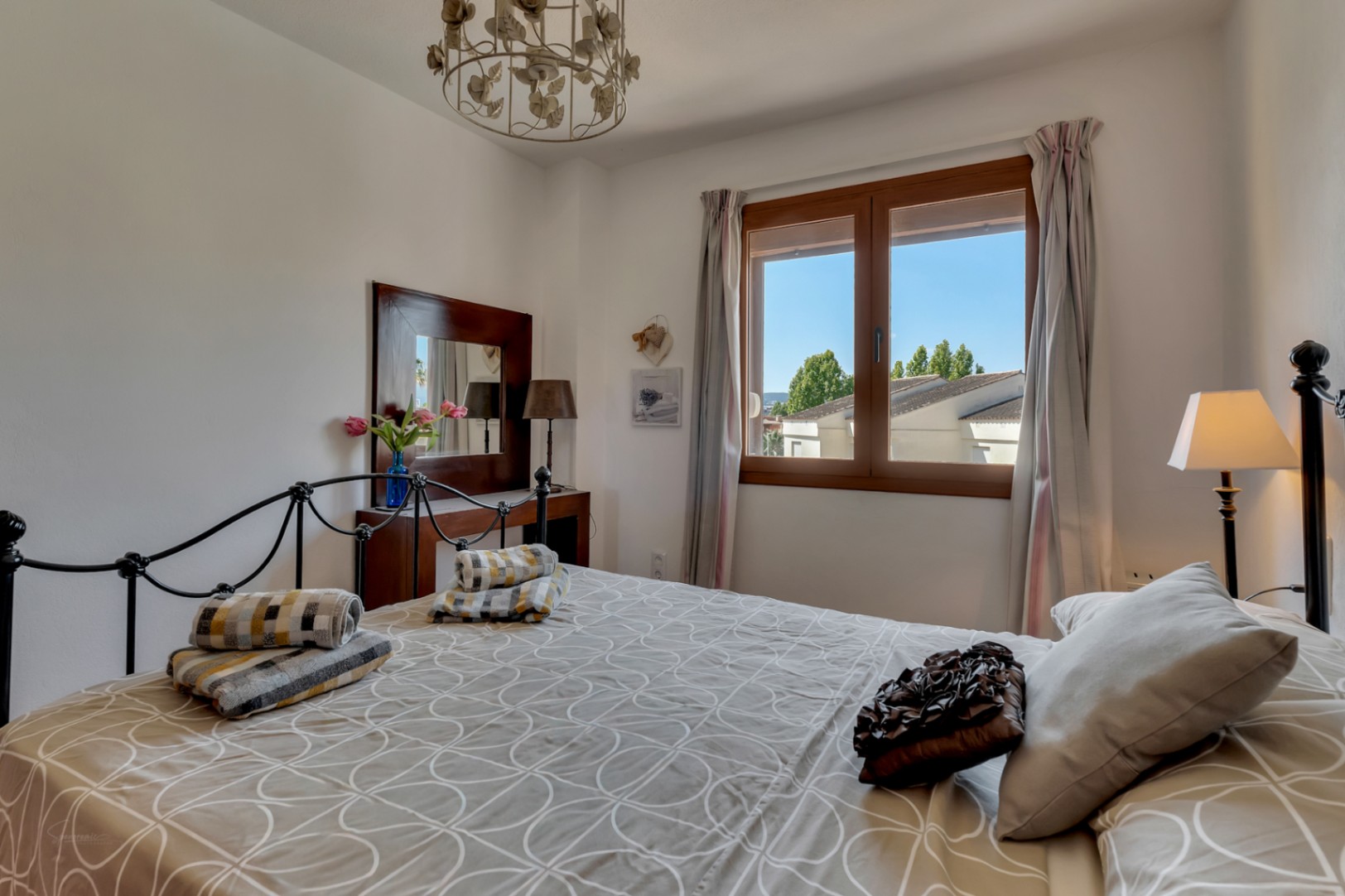 Chambre lumineuse avec lit en fer forgé, coiffeuse en bois foncé et fenêtre avec vue sur l'extérieur.