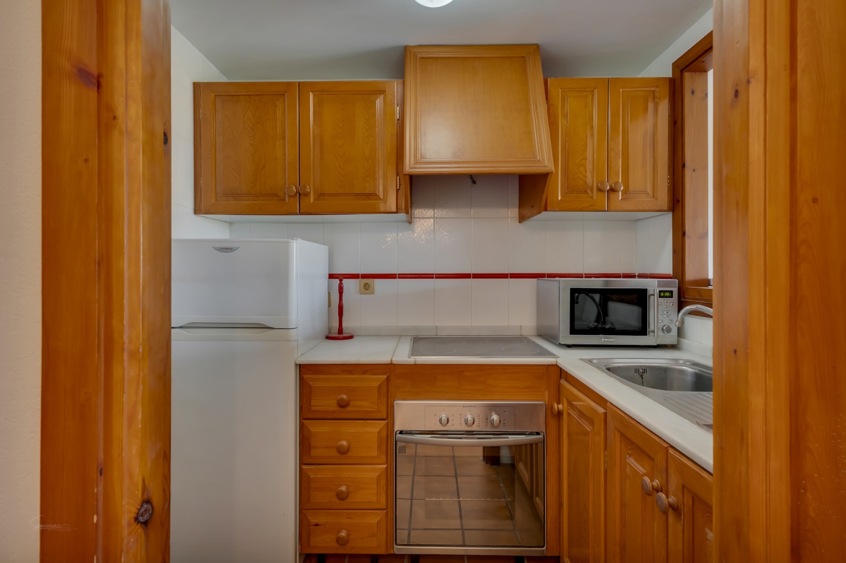 Cuisine compacte avec meubles en bois, électroménager blanc et plan de travail clair.