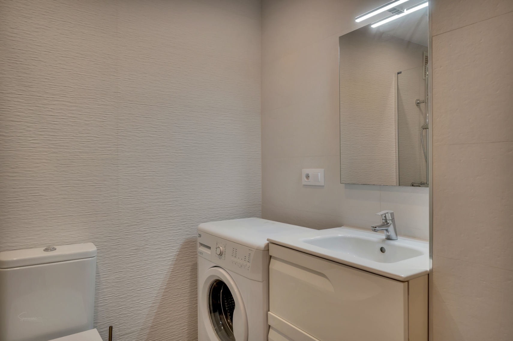 Détail de la salle de bain avec lavabo intégré, machine à laver et murs texturés dans des tons neutres.