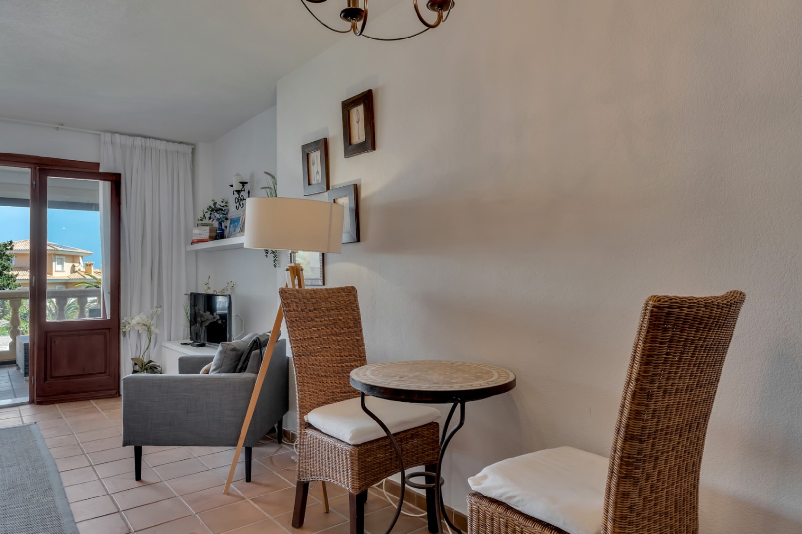Détail du salon avec table en mosaïque et chaises en osier, éclairé par un lampadaire.