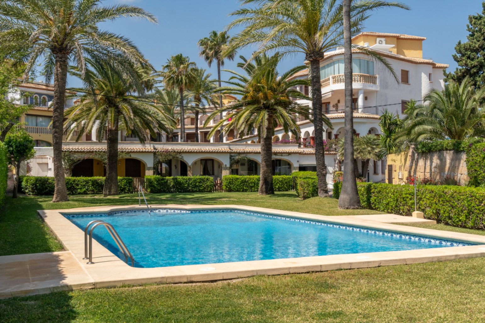 Piscine commune avec pelouse et palmiers dans une résidence à Jávea.
