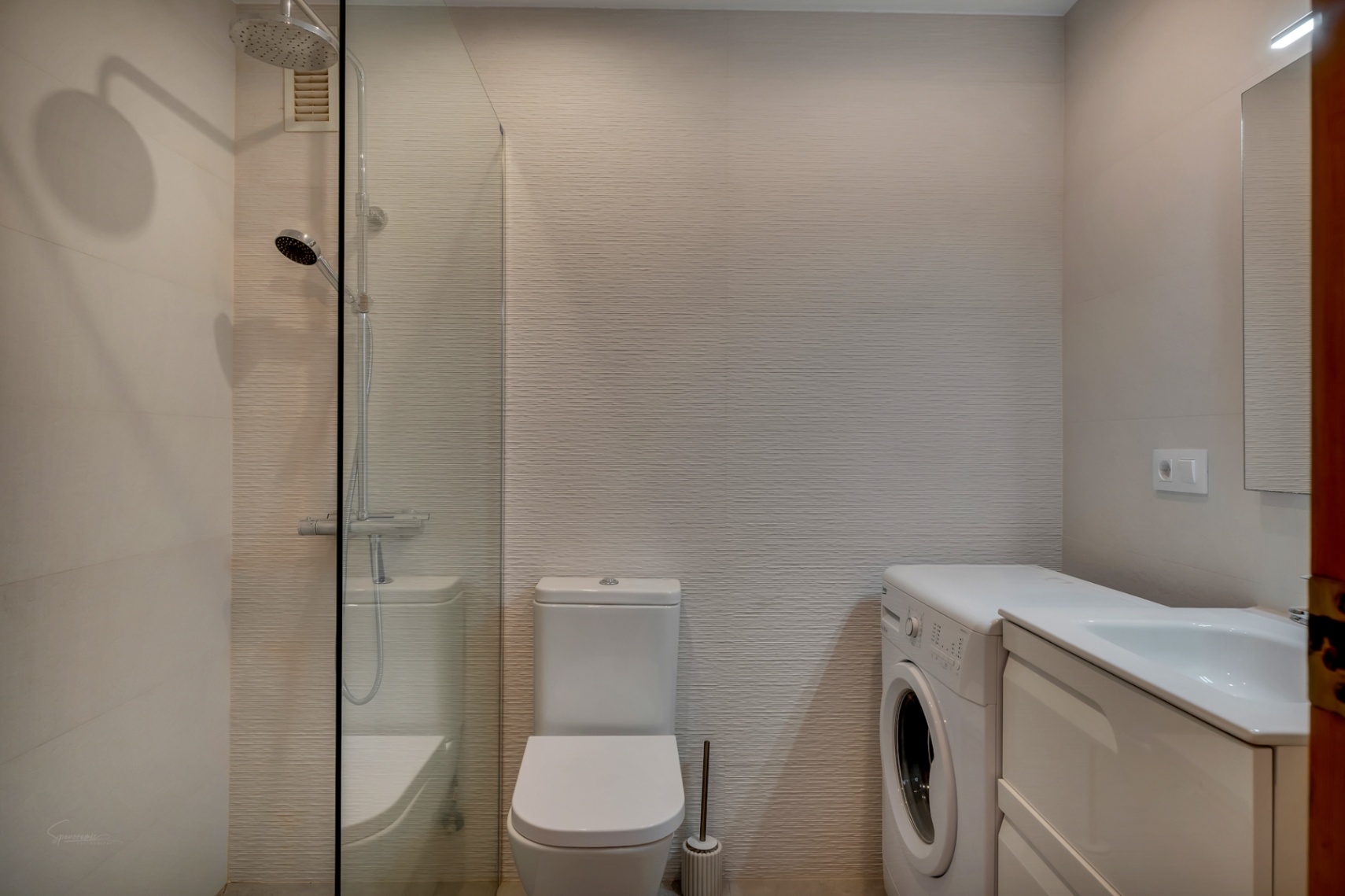 Salle de bain avec douche en verre, WC blanc, machine à laver et meuble-lavabo blanc.