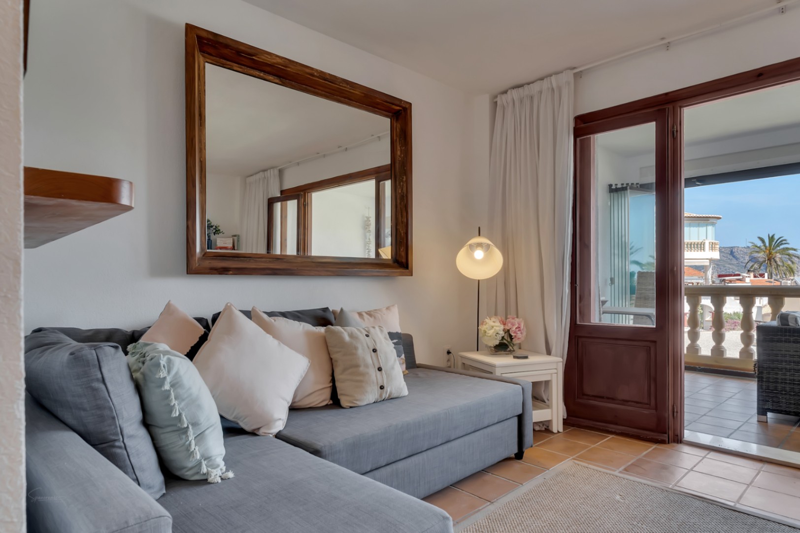 Salon avec canapé gris modulable, miroir encadré en bois et accès à la terrasse avec vue.