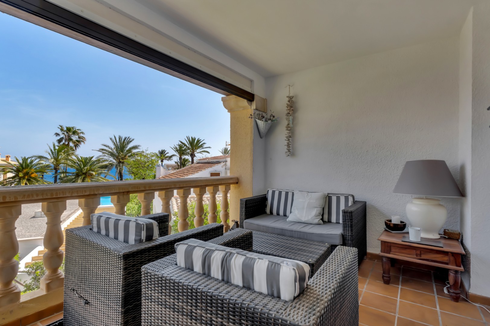 Terrasse avec vue sur mer, meublée de fauteuils en osier et coussins rayés, idéale pour la détente.