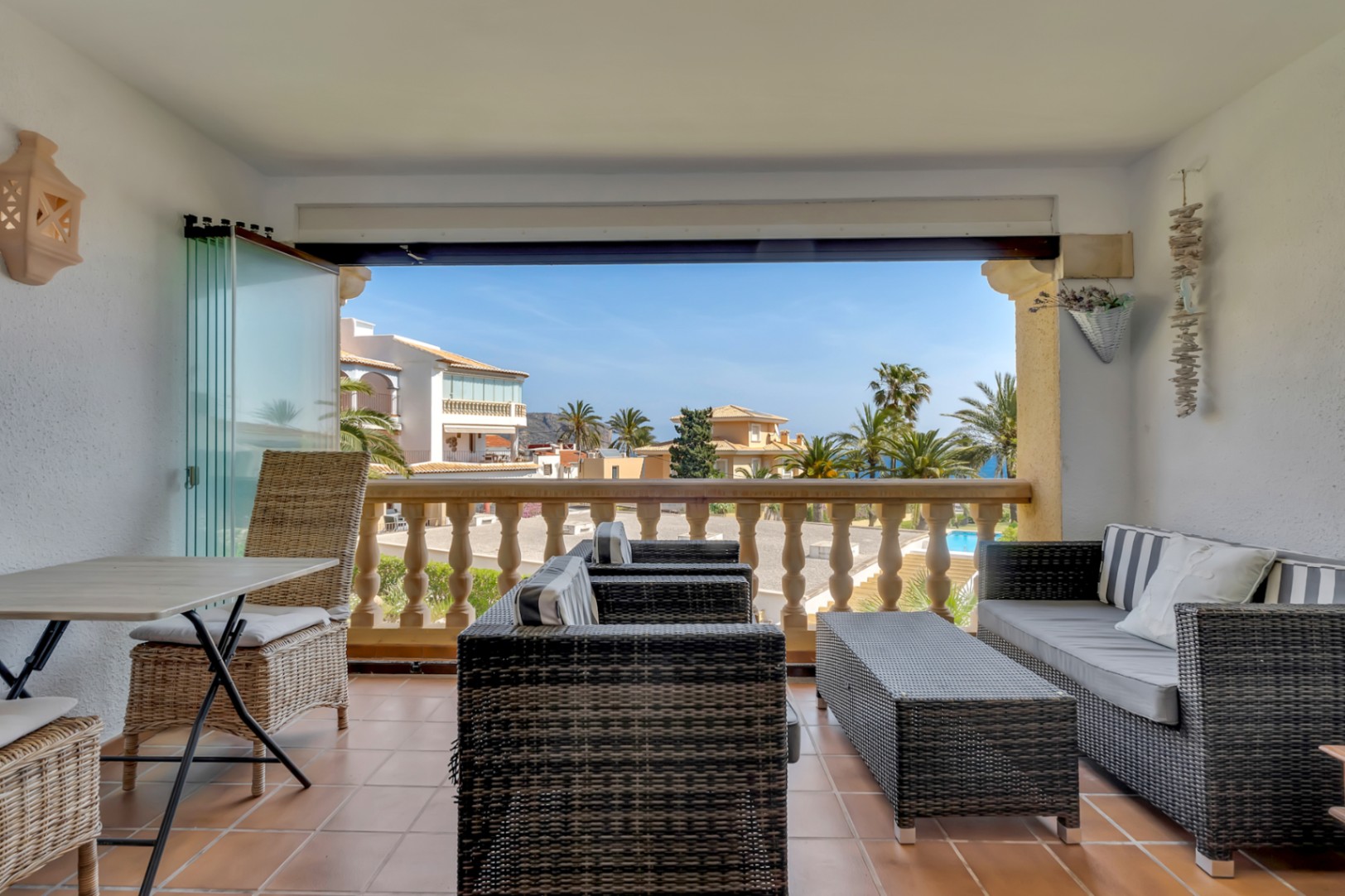 Terrasse vitrée avec mobilier en osier et vue sur la résidence et la mer.