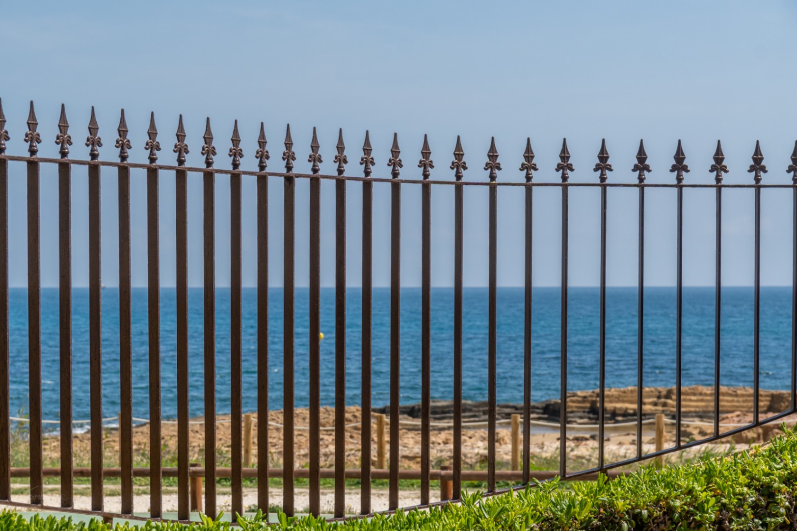 Vue sur la mer Méditerranée à travers une clôture en fer forgé avec détails ornementaux.