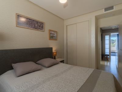 Chambre avec lit double, tête de lit en tissu, armoire intégrée et papier peint à motifs. Une ventilation de climatisation et un couloir lumineux vers l'extérieur sont visibles.