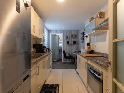 Cuisine en couloir équipée d'armoires claires, de comptoirs en granit et d'appareils électroménagers en acier inoxydable, dont un réfrigérateur et un four. Un petit coin repas est visible au fond.